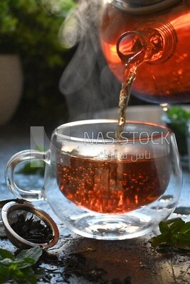 Glass kettle pouring tea from jug to cup of tea