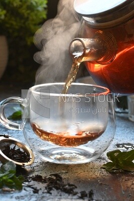 Glass kettle pouring tea from jug to cup of tea
