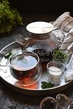 Cup of tea with a glass kettle, sugar, and a mint on a tray