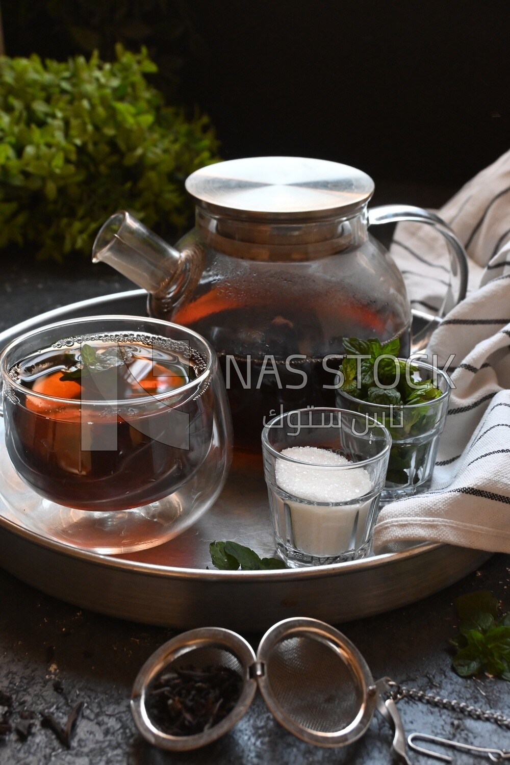 Cup of tea with a glass kettle, sugar, and a mint on a tray