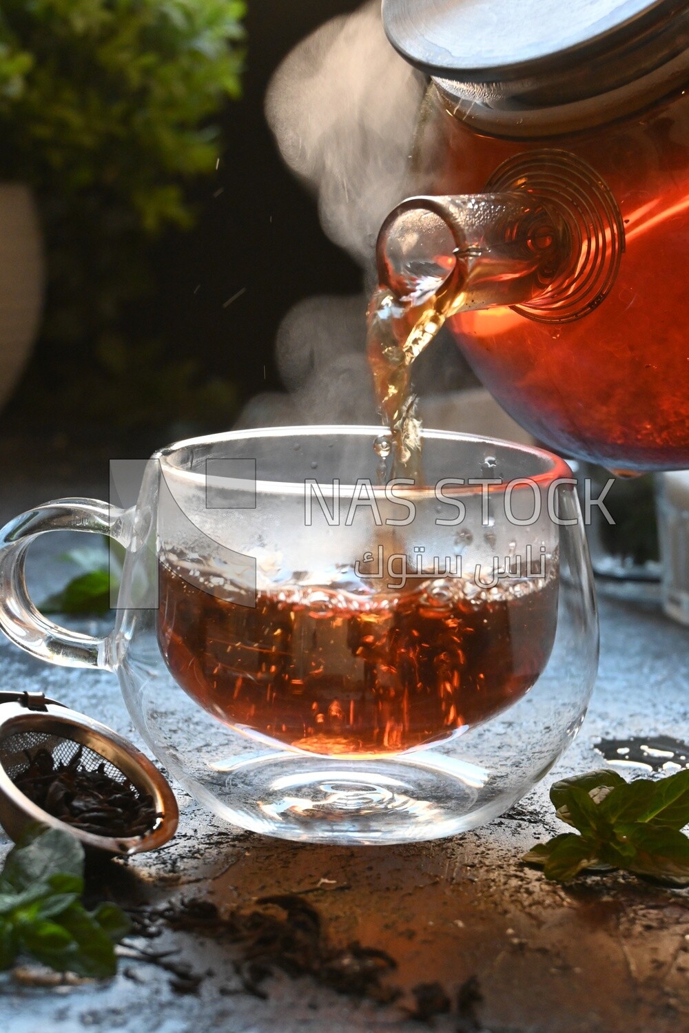 Glass kettle pouring tea from jug to cup of tea