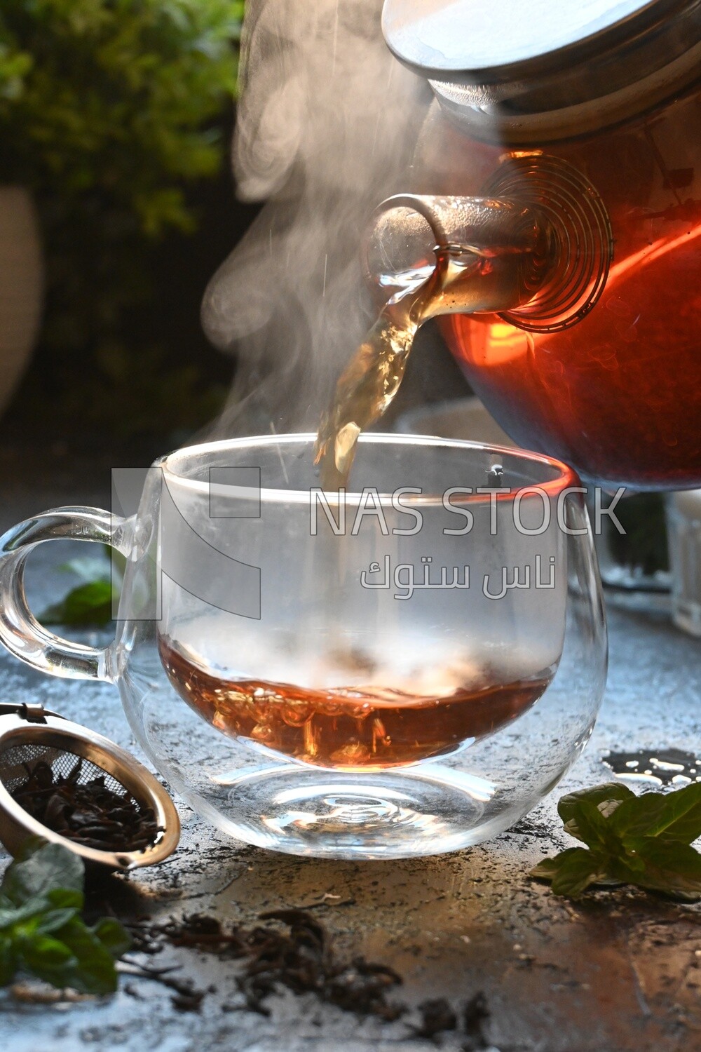 Glass kettle pouring tea from jug to cup of tea