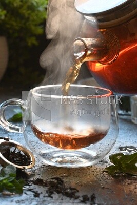 Glass kettle pouring tea from jug to cup of tea