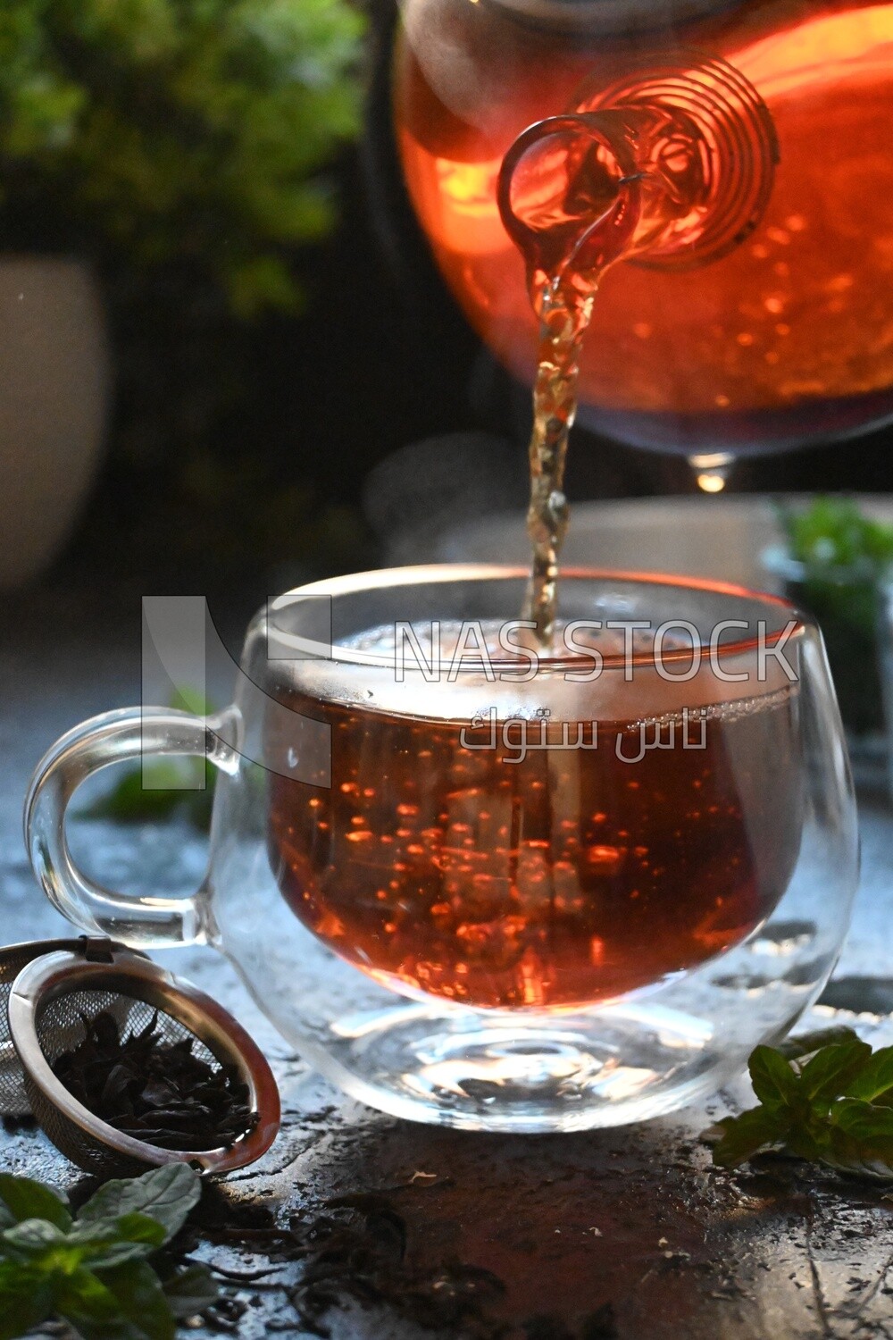 Glass kettle pouring tea from jug to cup of tea