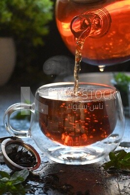Glass kettle pouring tea from jug to cup of tea