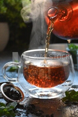 Glass kettle pouring tea from jug to cup of tea