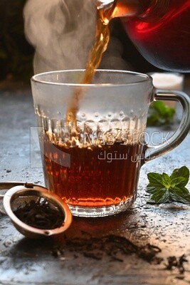 Glass kettle pouring tea from jug to cup of tea
