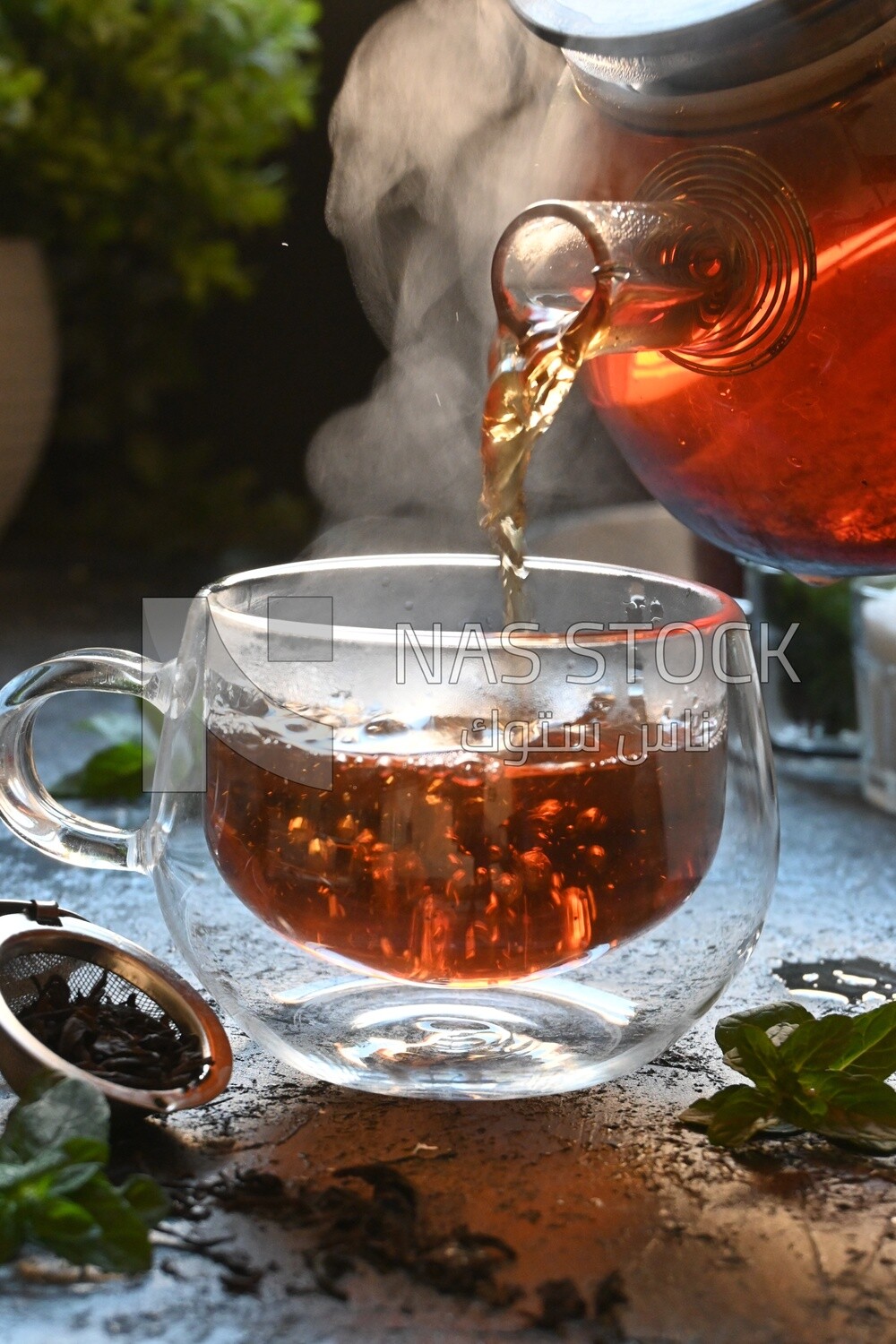 Glass kettle pouring tea from jug to cup of tea