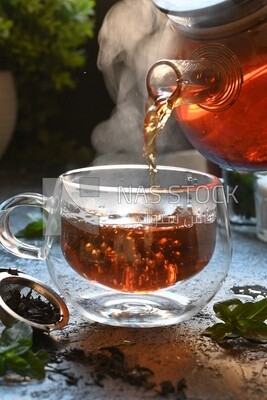 Glass kettle pouring tea from jug to cup of tea