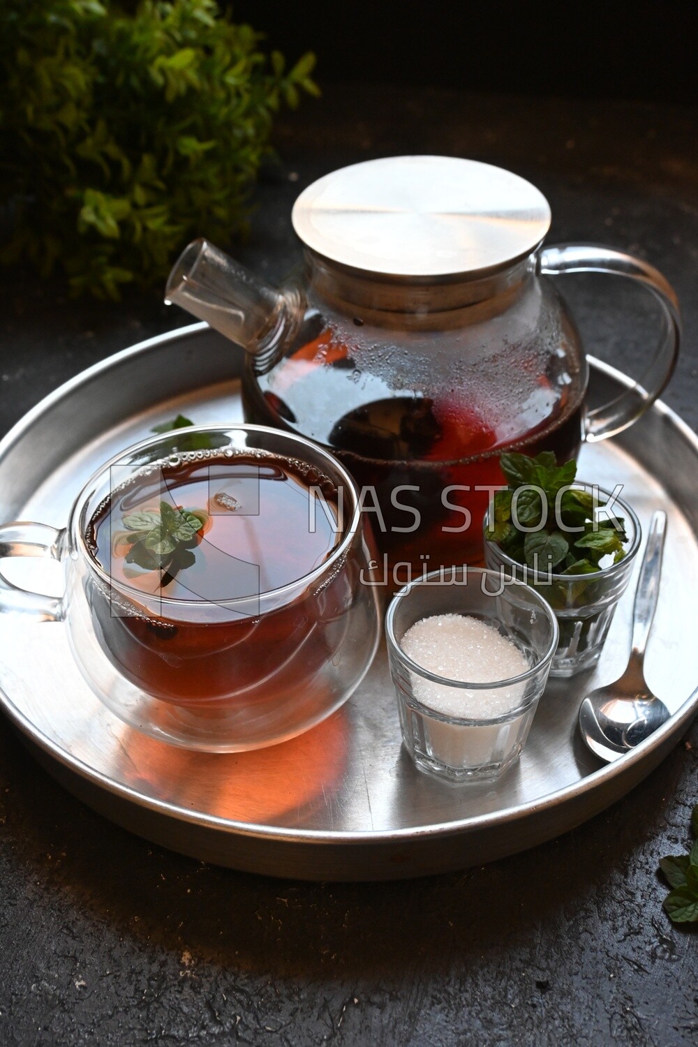 Cup of tea with a glass kettle, sugar, and a mint on a tray
