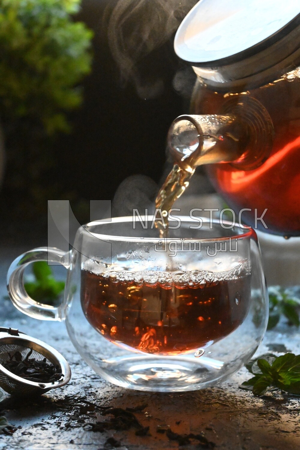Glass kettle pouring tea from jug to cup of tea