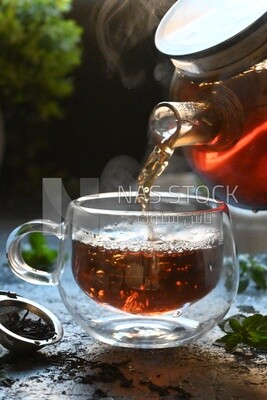 Glass kettle pouring tea from jug to cup of tea