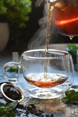 Glass kettle pouring tea from jug to cup of tea