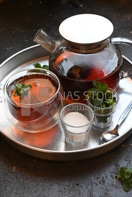 Cup of tea with a glass kettle, sugar, and a mint on a tray