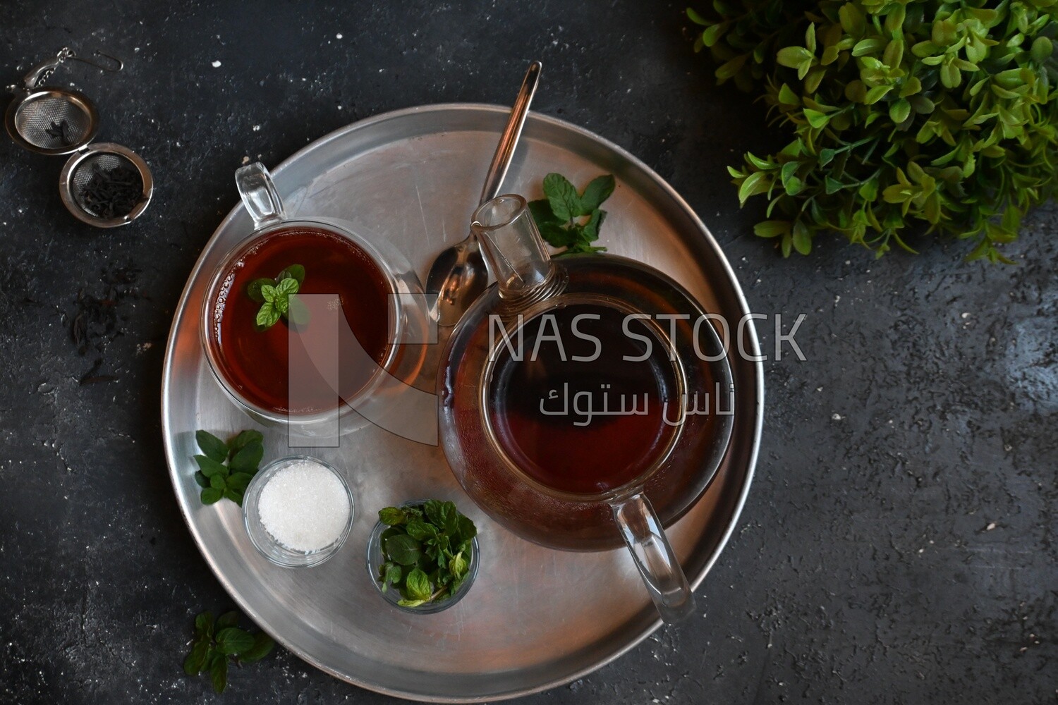 Cup of tea with a glass kettle, sugar, and a mint on a tray