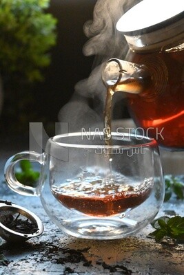 Glass kettle pouring tea from jug to cup of tea