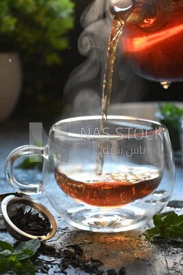 Glass kettle pouring tea from jug to cup of tea