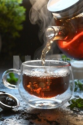 Glass kettle pouring tea from jug to cup of tea