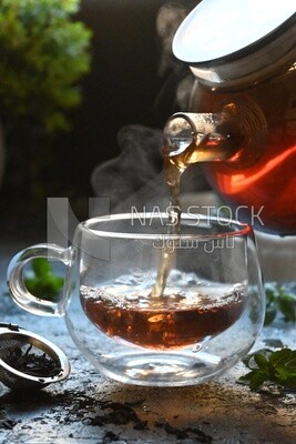 Glass kettle pouring tea from jug to cup of tea