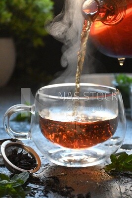 Glass kettle pouring tea from jug to cup of tea