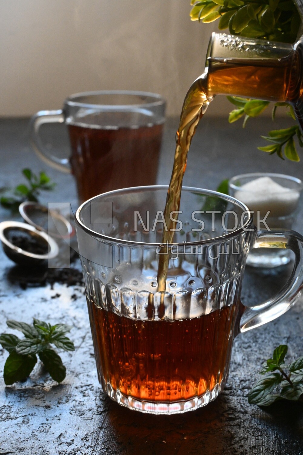 Glass kettle pouring tea from jug to cup of tea