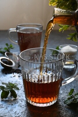 Glass kettle pouring tea from jug to cup of tea