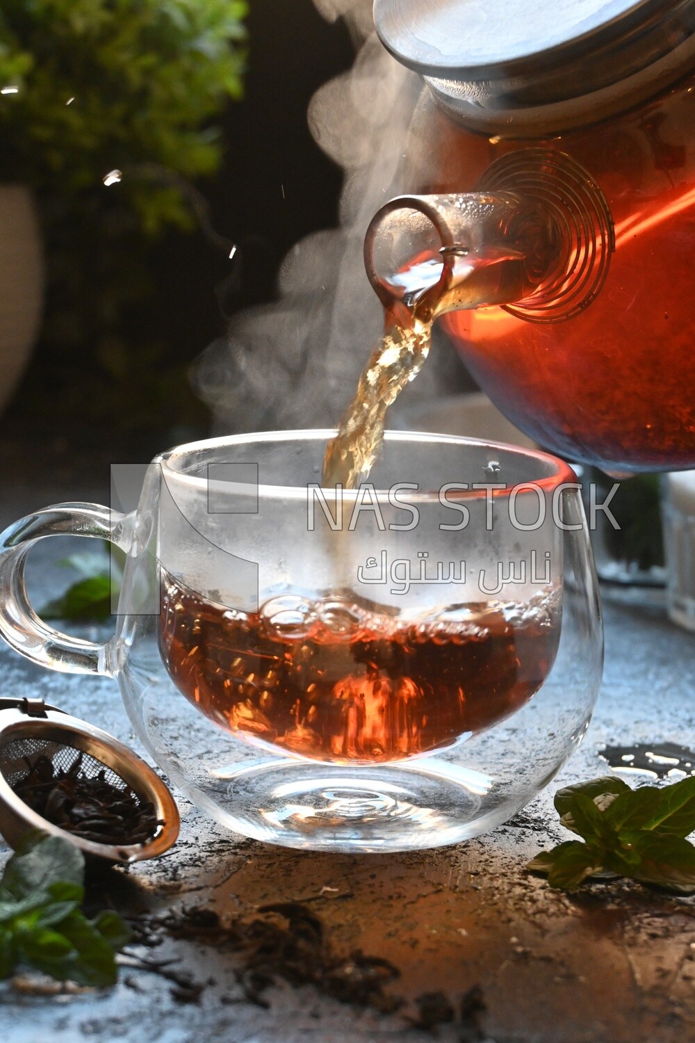 Glass kettle pouring tea from jug to cup of tea