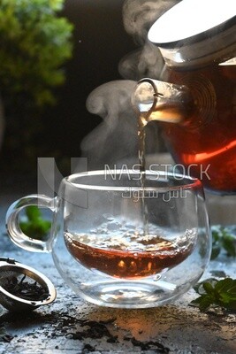Glass kettle pouring tea from jug to cup of tea