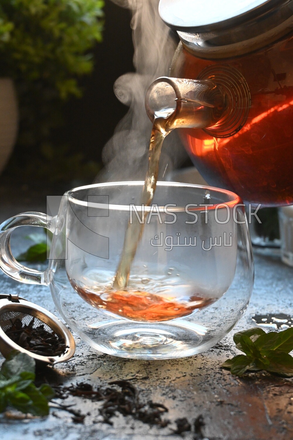 Glass kettle pouring tea from jug to cup of tea
