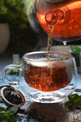 Glass kettle pouring tea from jug to cup of tea