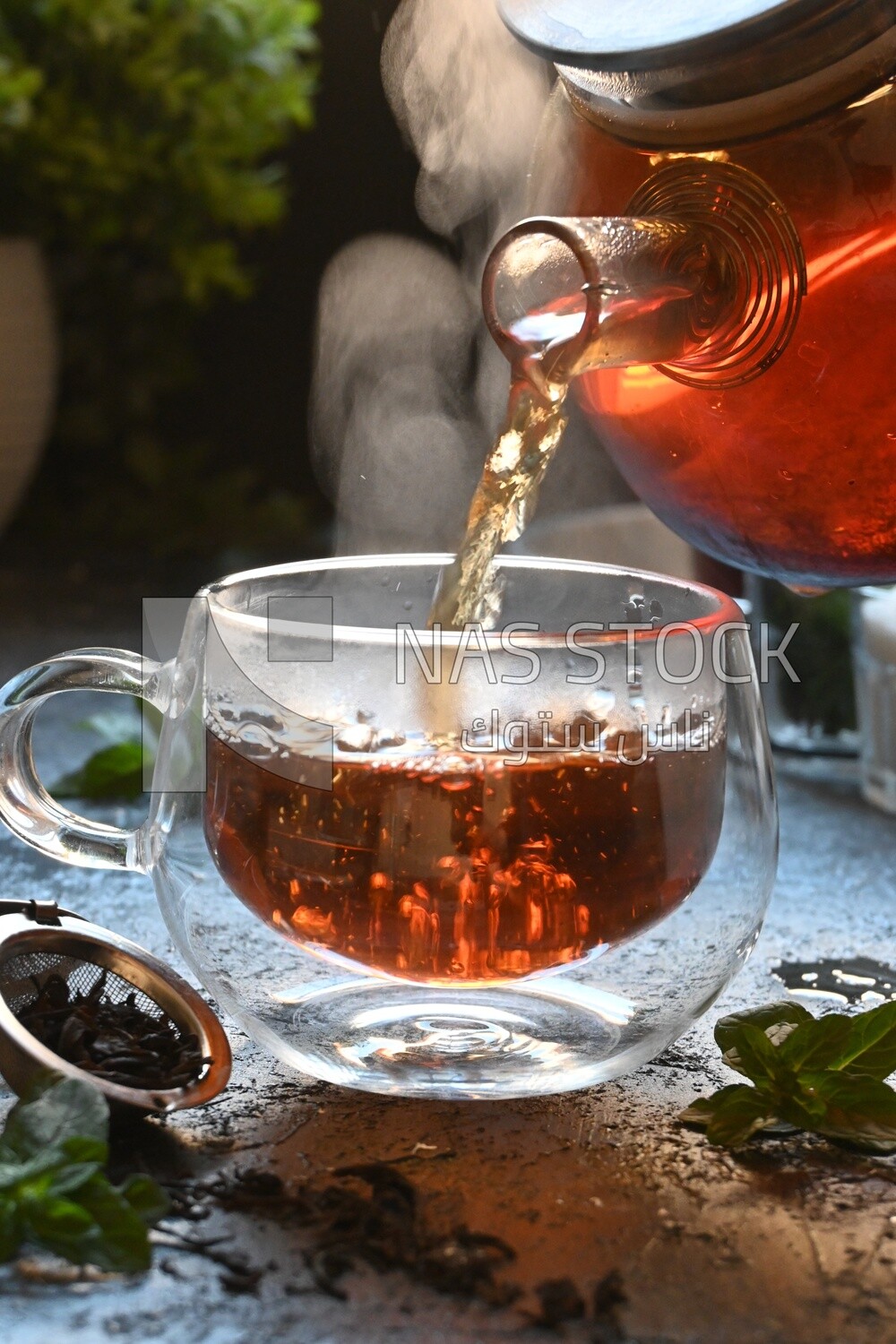 Glass kettle pouring tea from jug to cup of tea