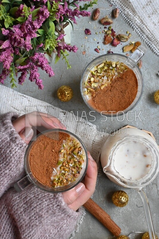 Hand holding a cup of sahlab with cinnamon and nuts on it