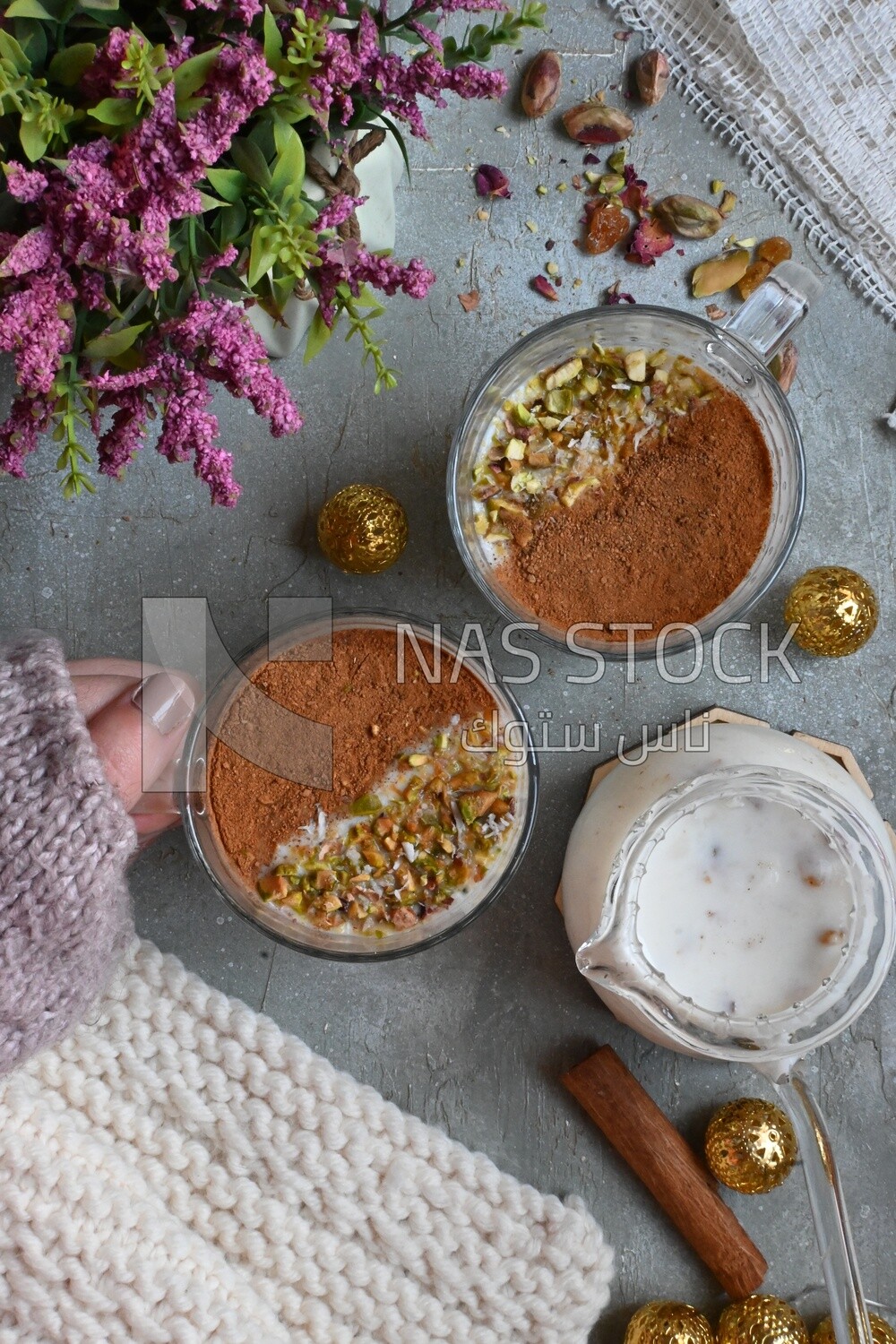 Hand holding a cup of sahlab with cinnamon and nuts on it