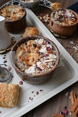 Plate of Umm Ali with nuts on it, cinnamon sticks, famous oriental Arabic sweets, bread and milk sweets