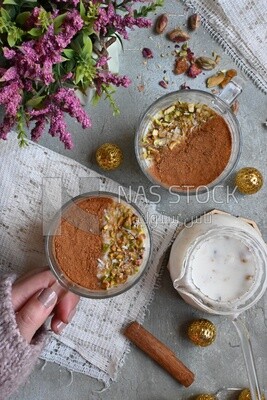 Hand holding a cup of sahlab with cinnamon and nuts on it