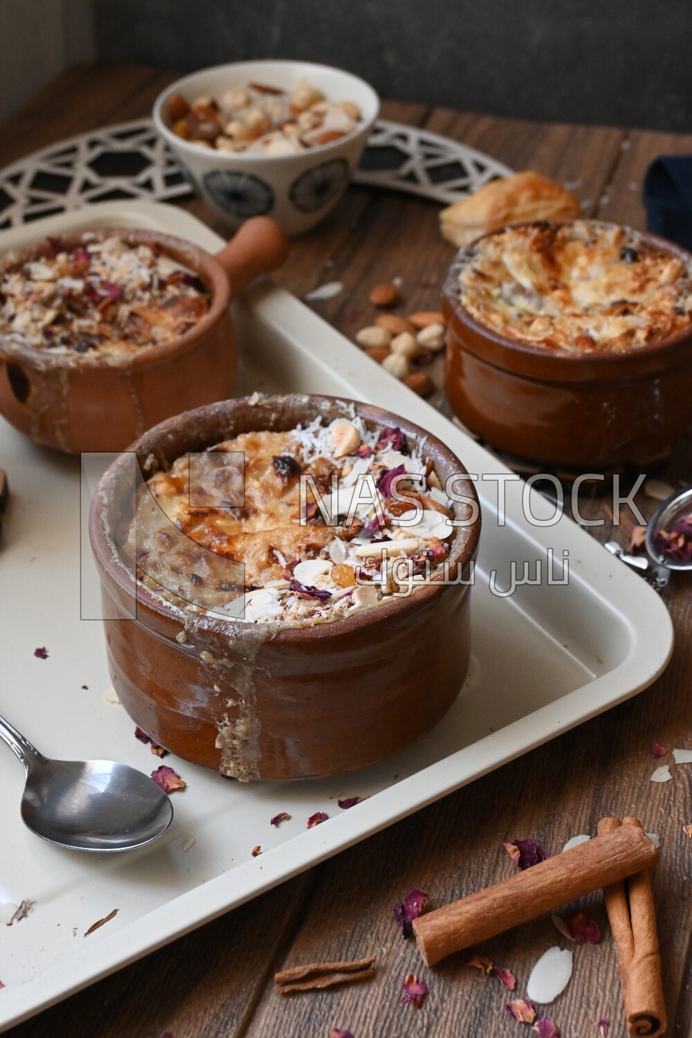 Plate of Umm Ali with nuts on it, cinnamon sticks, famous oriental Arabic sweets, bread and milk sweets