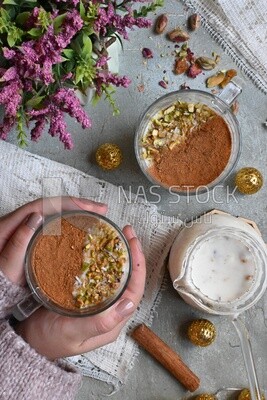 Hand holding a cup of sahlab with cinnamon and nuts on it