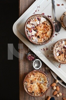 Top view of a plate of Umm Ali with nuts on it, cinnamon sticks, famous oriental Arabic sweets, bread and milk sweets