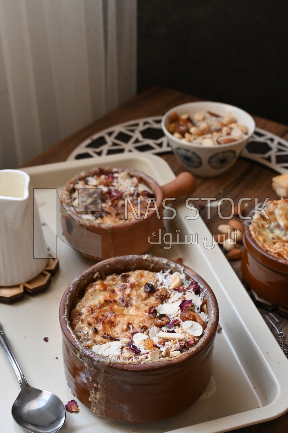 Top view of a plate of Umm Ali with nuts on it, cinnamon sticks, famous oriental Arabic sweets, bread and milk sweets