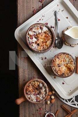 Top view of a plate of Umm Ali with nuts on it, cinnamon sticks, famous oriental Arabic sweets, bread and milk sweets