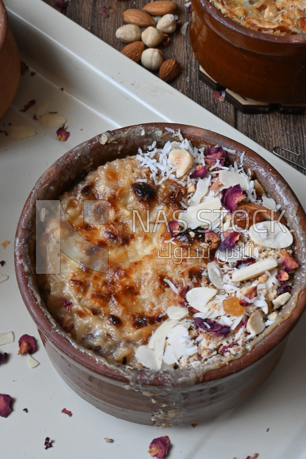 Plate of Umm Ali with nuts on it, cinnamon sticks, famous oriental Arabic sweets, bread and milk sweets