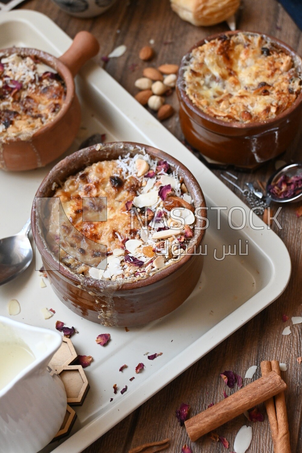 Plate of Umm Ali with nuts on it, cinnamon sticks, famous oriental Arabic sweets, bread and milk sweets
