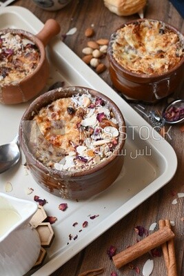 Plate of Umm Ali with nuts on it, cinnamon sticks, famous oriental Arabic sweets, bread and milk sweets
