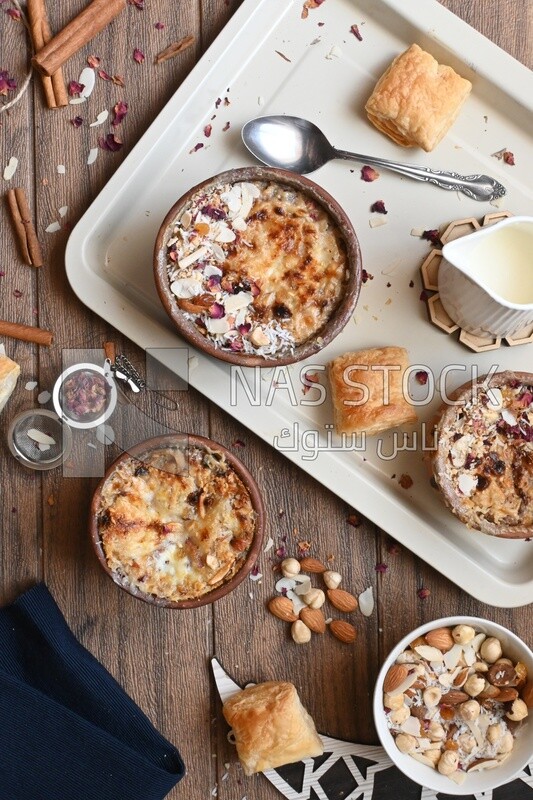 Top view of a plate of Umm Ali with nuts on it, cinnamon sticks, famous oriental Arabic sweets, bread and milk sweets