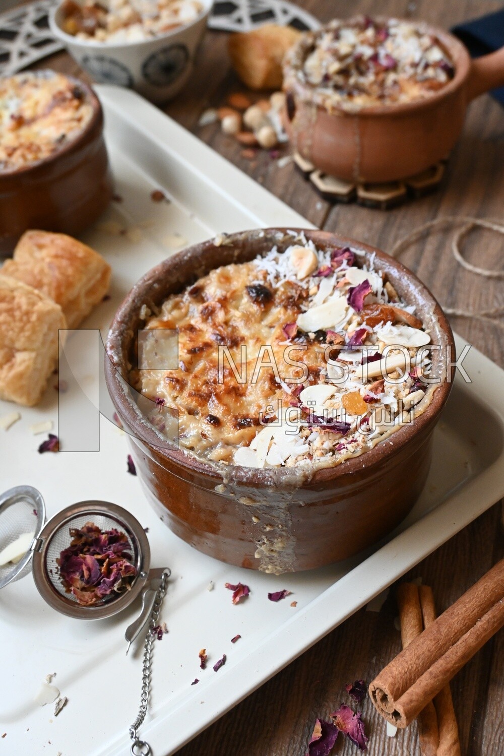 Plate of Umm Ali with nuts on it, cinnamon sticks, famous oriental Arabic sweets, bread and milk sweets