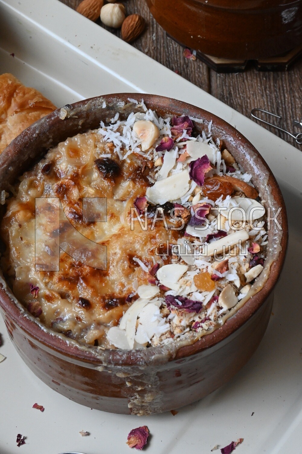 Close up of a plate of Umm Ali with nuts on it, cinnamon sticks, famous oriental Arabic sweets, bread and milk sweets