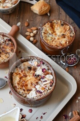 Plate of Umm Ali with nuts on it, cinnamon sticks, famous oriental Arabic sweets, bread and milk sweets