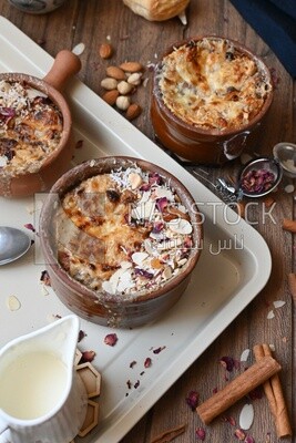 Plate of Umm Ali with nuts on it, cinnamon sticks, famous oriental Arabic sweets, bread and milk sweets