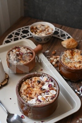 Plate of Umm Ali with nuts on it, cinnamon sticks, famous oriental Arabic sweets, bread and milk sweets