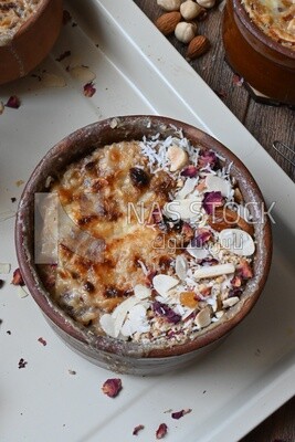 Top view of a plate of Umm Ali with nuts on it, cinnamon sticks, famous oriental Arabic sweets, bread and milk sweets